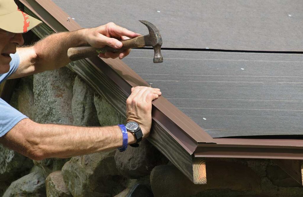 Workers protect a shingled roof with padded walk boards while remodeling an exterior wall.
