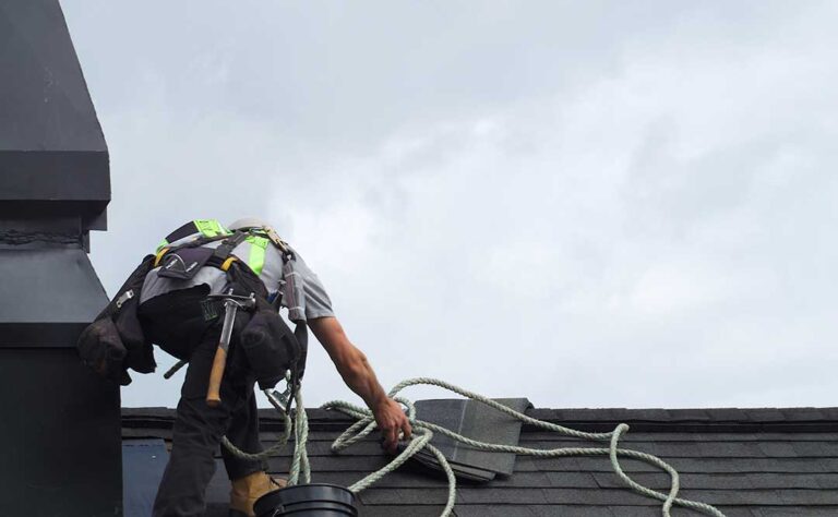 A homeowner examines damaged shingles and flashing beside a roof leak during a careful inspection.